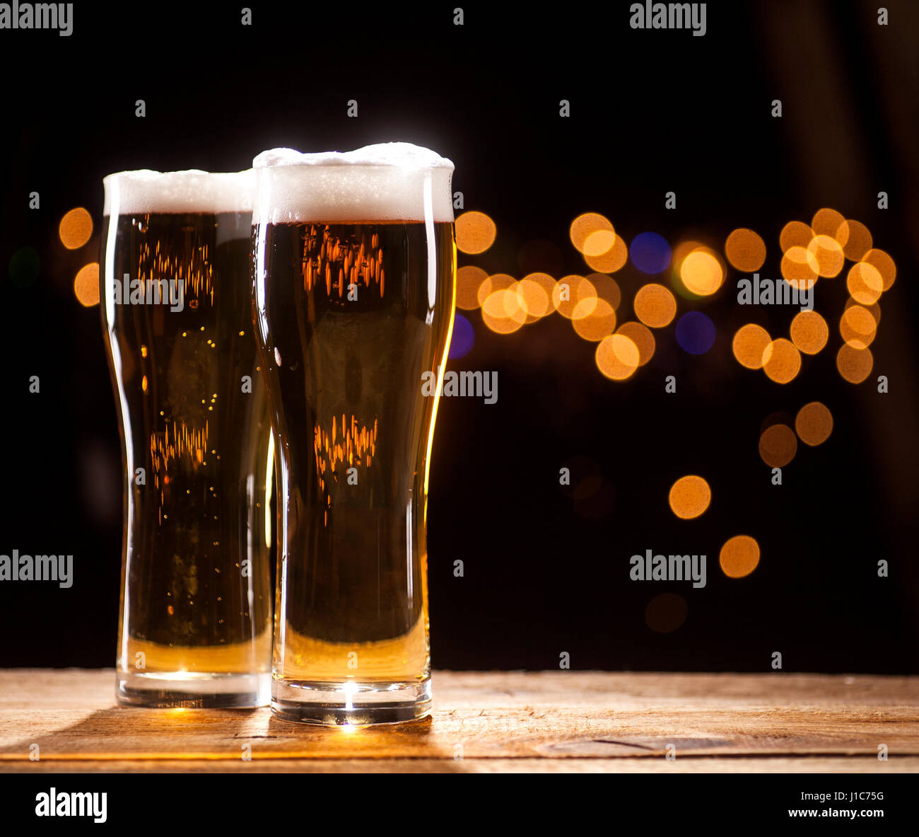 Due bicchieri di birra sul tavolo di legno e le luci della barra sfondo. Foto Stock Due bicchieri di birra sul tavolo di legno e le luci della barra sfondo. Foto Stock