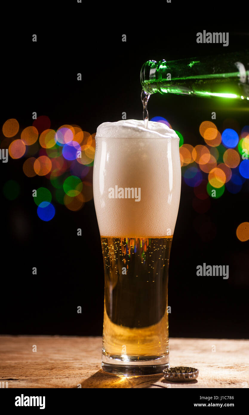 La birra è di colare in vetro su un tavolo di legno e le luci della barra sfondo. Foto Stock La birra è di colare in vetro su un tavolo di legno e le luci della barra sfondo. Foto Stock