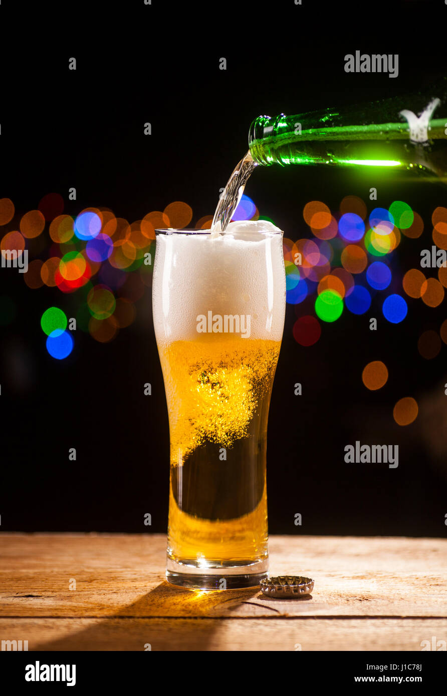 La birra è di colare in vetro su un tavolo di legno e le luci della barra sfondo. Foto Stock La birra è di colare in vetro su un tavolo di legno e le luci della barra sfondo. Foto Stock