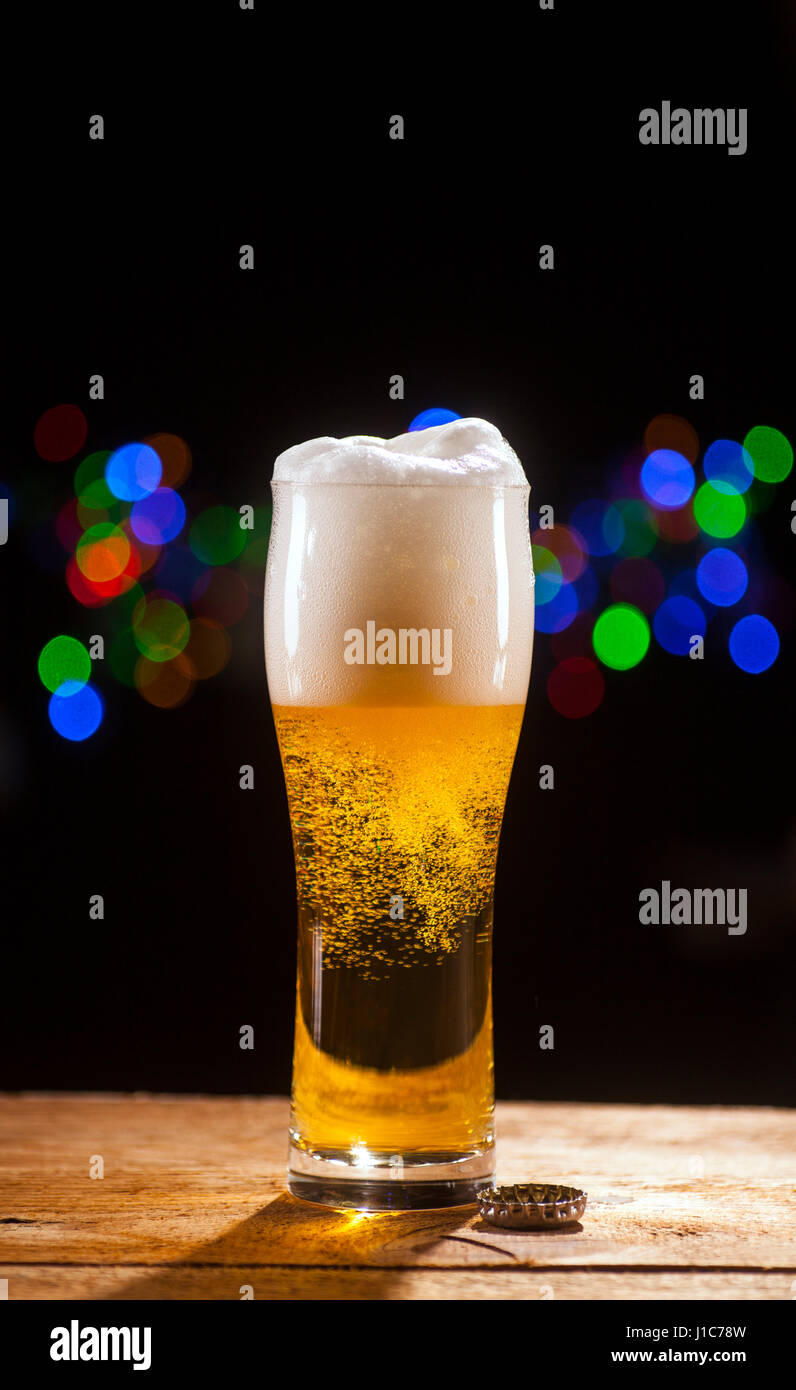 Bicchiere di birra sul tavolo di legno e le luci della barra sfondo. Foto Stock Bicchiere di birra sul tavolo di legno e le luci della barra sfondo. Foto Stock