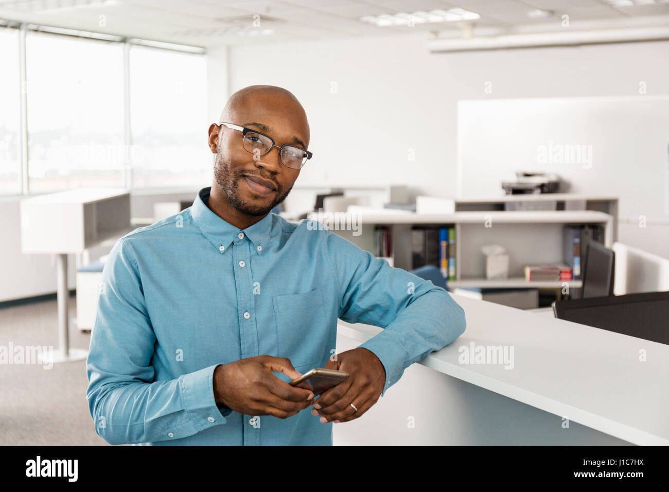 Sorridente African American uomo sms sul cellulare in ufficio Foto Stock