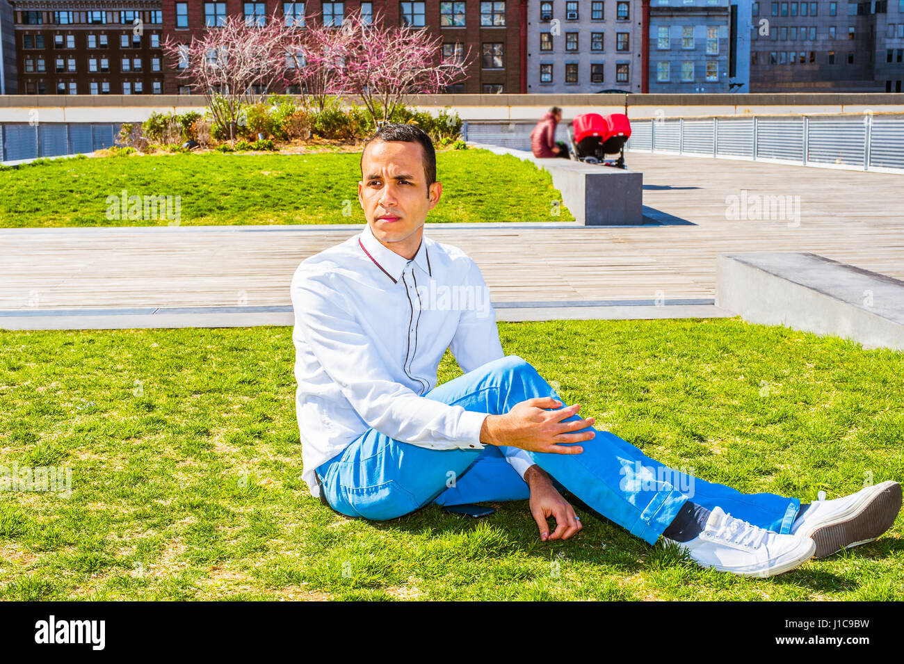 Giovane uomo americano che indossa una camicia bianca e pantaloni blu,  bianco sneakers, seduto sul prato verde a Park di New York, pensando. Donna  con passeggini per bambini Foto stock - Alamy