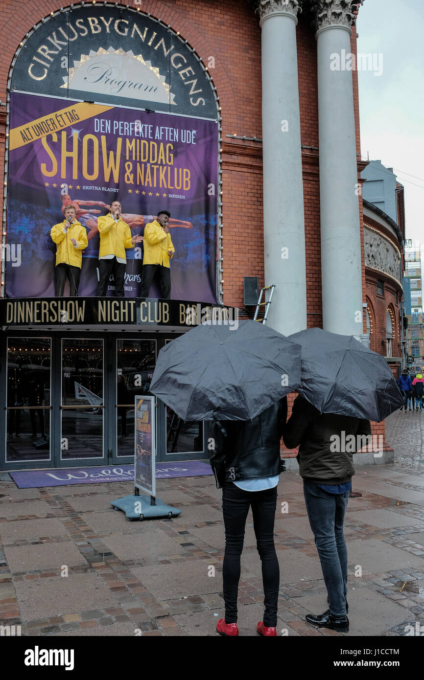 Cantando sotto la pioggia, tre animatori in giallo raincoats promuovere una mostra a Cirkusbygningen, un XIX secolo edificio circolare, Copenhagen, Danimarca Foto Stock