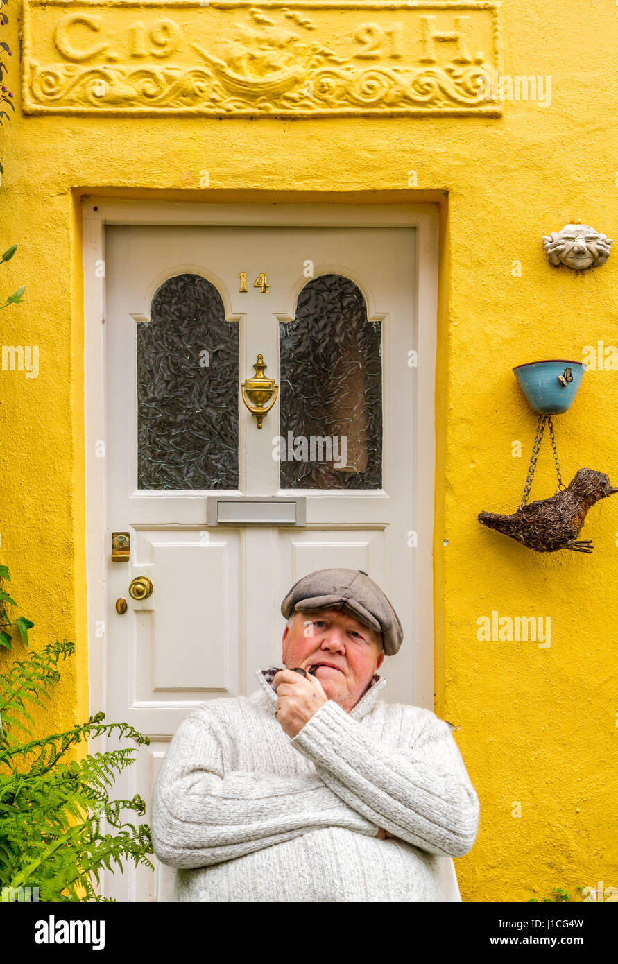 Clovelly,Devon, Inghilterra, un residente di questo pittoresco villaggio in North Devon gode di seduta al di fuori del suo dipinto luminosamente cottage fumare la pipa.UK Foto Stock