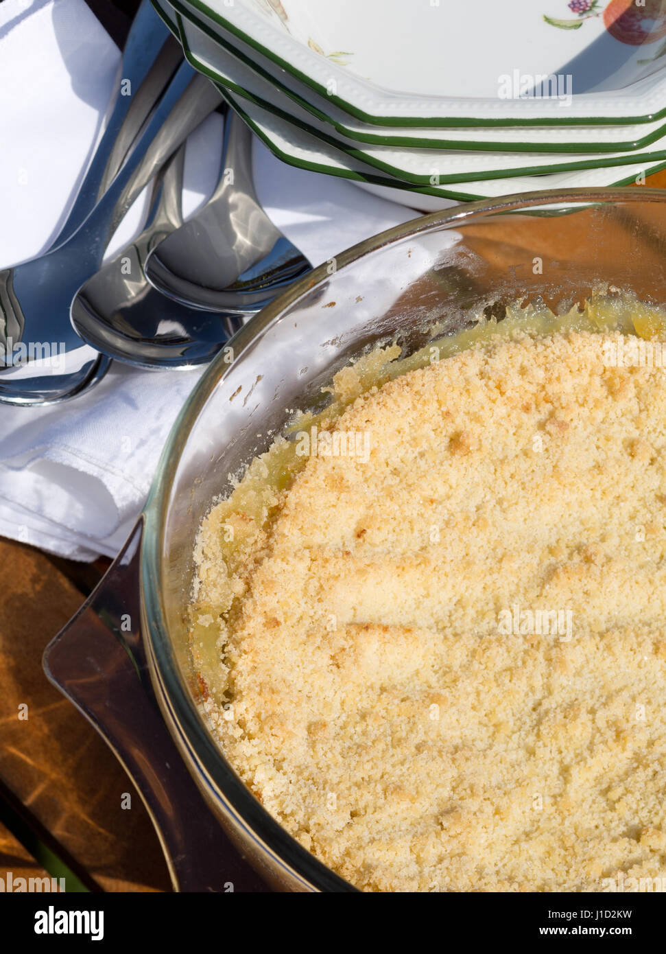 Home ha fatto apple crumble cotte nel recipiente di vetro, con cucchiai di portata e piatti del deserto dietro. Foto Stock
