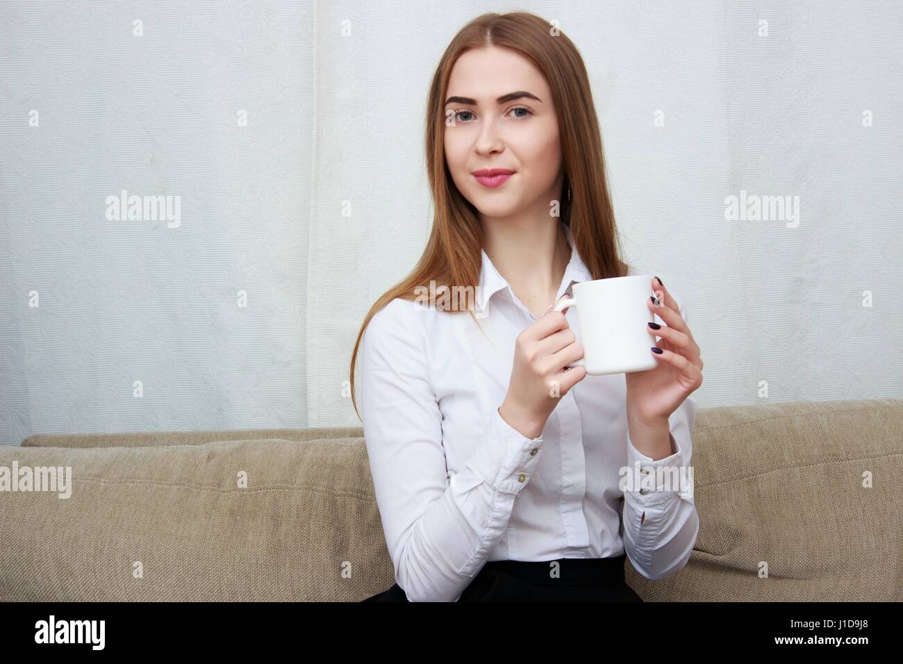 Giovane bella ragazza con tazza di caffè seduti sul divano di casa. Foto Stock