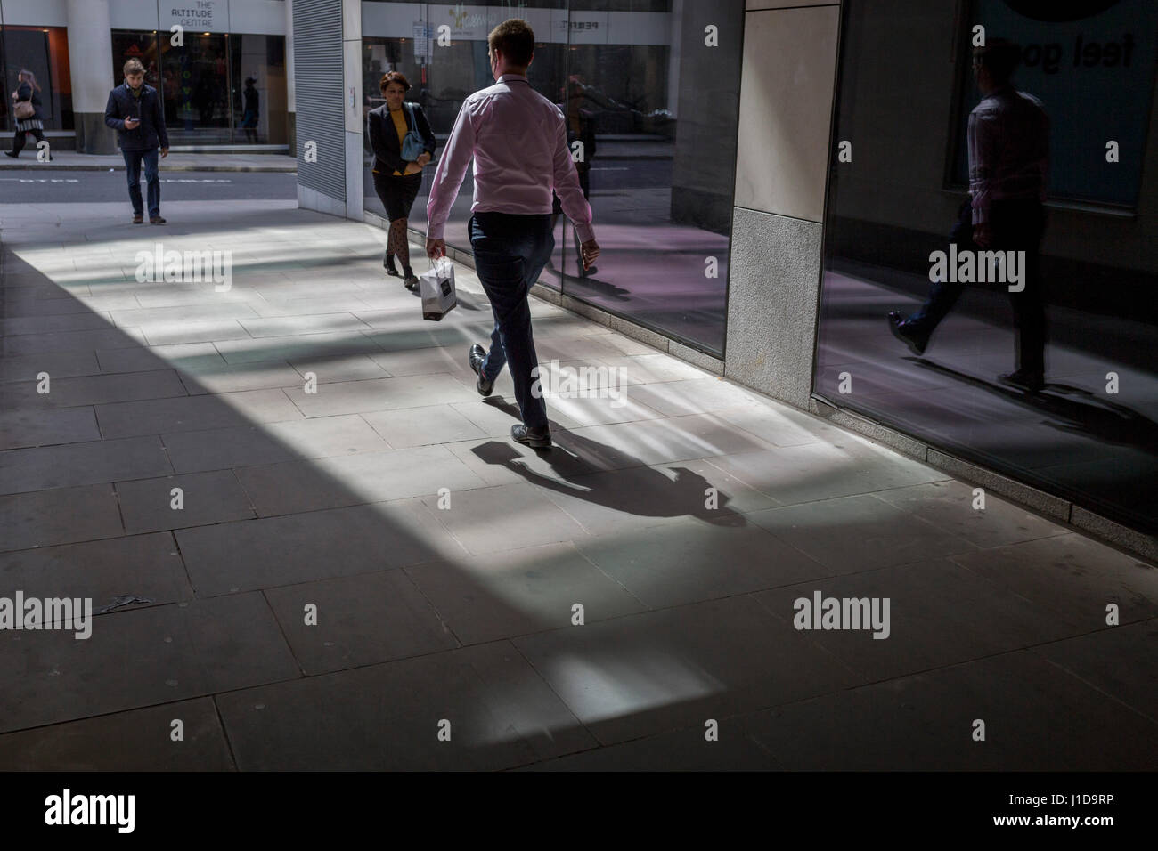 I lavoratori della città a piedi attraverso un passaggio pedonale coperto dove la luce riflessa dall'ufficio di lastra di vetro lascia ombre, il 19 aprile, nella City di Londra, Foto Stock
