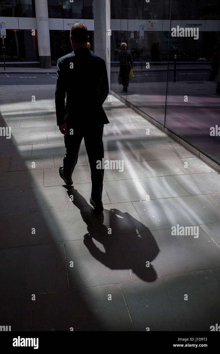 I lavoratori della città a piedi attraverso un passaggio pedonale coperto dove la luce riflessa dall'ufficio di lastra di vetro lascia ombre, il 19 aprile, nella City di Londra, Foto Stock