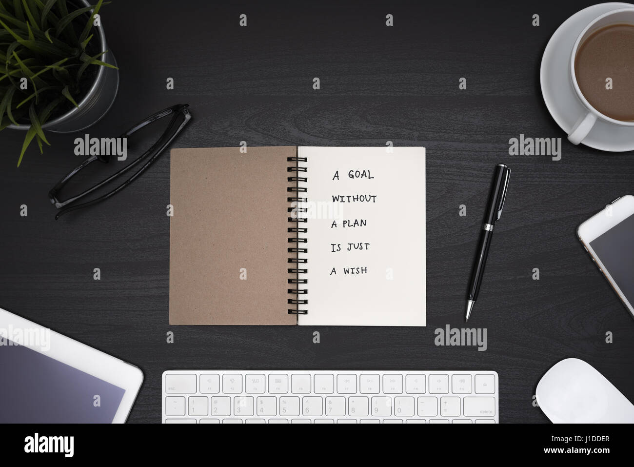 Un obiettivo senza un piano è solo un desiderio motivazionali di calligrafia su notebook con computer, forniture da ufficio e la tazza di caffè sulla scrivania nero tabella, parte superiore Foto Stock