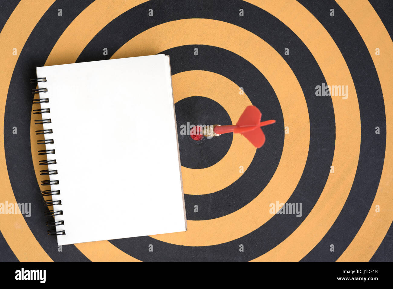 La freccia che colpisce in bullseye target su dartboard con spirale aperta notebook Foto Stock
