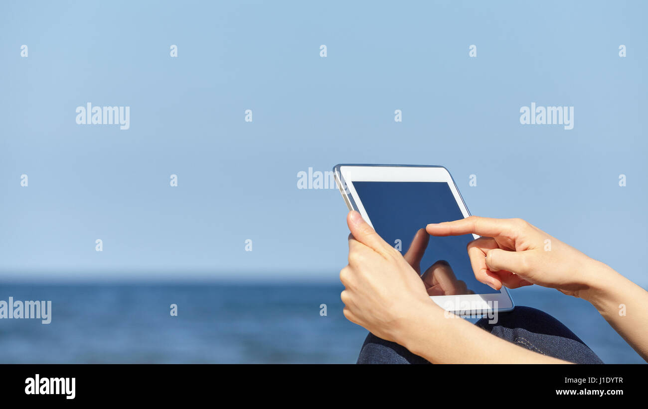 Chiudere l immagine del dito femmina di toccare lo schermo del tablet pc su una spiaggia, il fuoco selettivo, spazio per il testo. Foto Stock