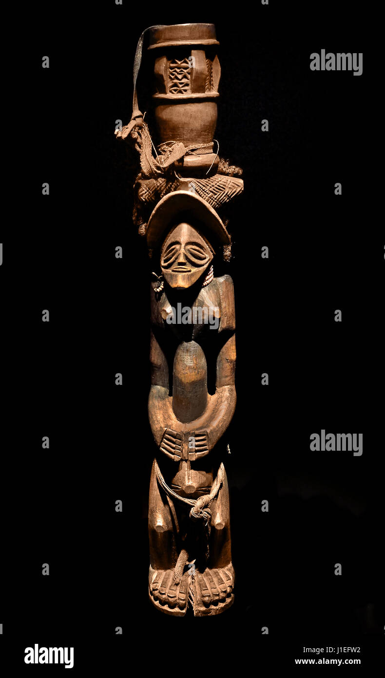 Questa immagine presenta una figura o standard del tradizionale suonatore di tamburi Chokwe del XIX secolo, molto rara e magistralmente scolpita, creata da un artigiano dell'Angola o dai confini della Repubblica Democratica del Congo e dello Zambia. Lo standard di legno Chokwe raffigura una figura in piedi che bilancia un tamburo cerimoniale sulla testa, una scultura dell'Africa centro-occidentale isolata su uno sfondo nero Foto Stock