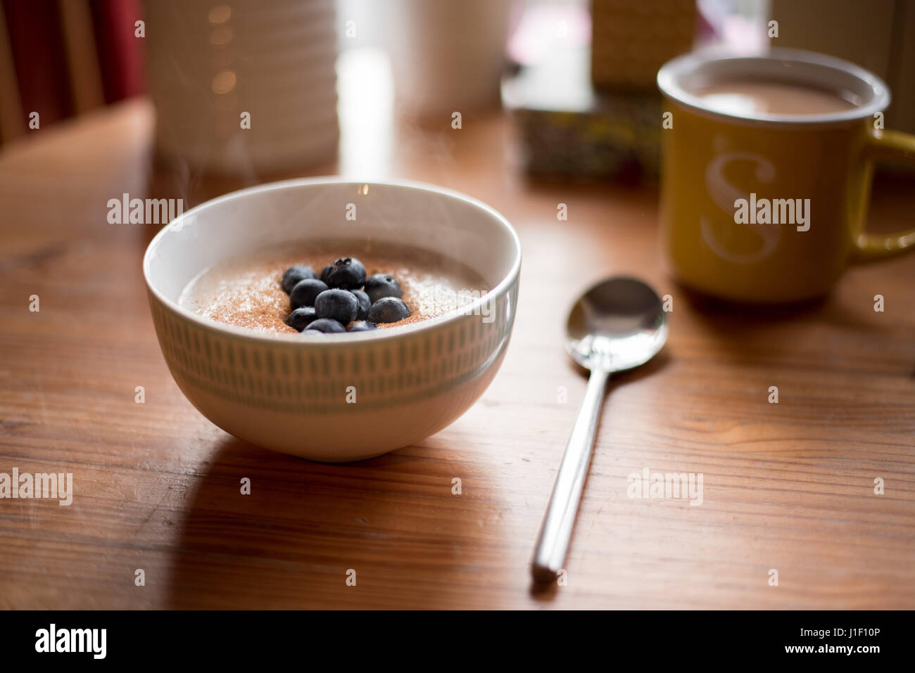 Il recipiente per la cottura a vapore di porridge nel tavolo per la colazione in scena con la tazza di tè. Foto Stock