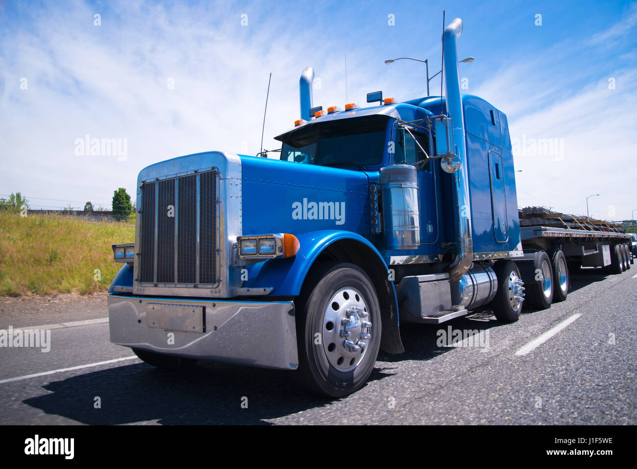 Blu classico normale big rig semi carrello cromato con accessori e dettagli su una autostrada multilane road con un carico pianale rimorchio su sfondo Foto Stock