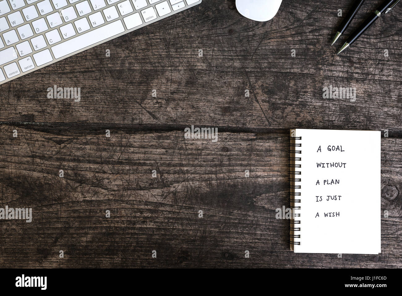 Un obiettivo senza un piano è solo un desiderio motivazionali di scrittura a mano su un notebook con mouse e tastiera la penna sulla grungy tabella Foto Stock
