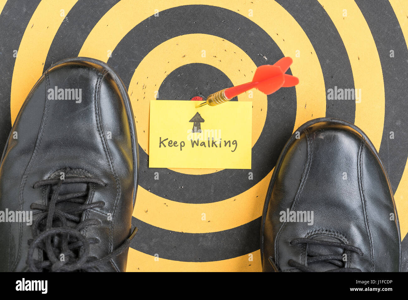 Vista superiore del nero scarpe su dartboard con la parola manoscritta continuare a camminare in una nota adesiva, il successo aziendale concept Foto Stock