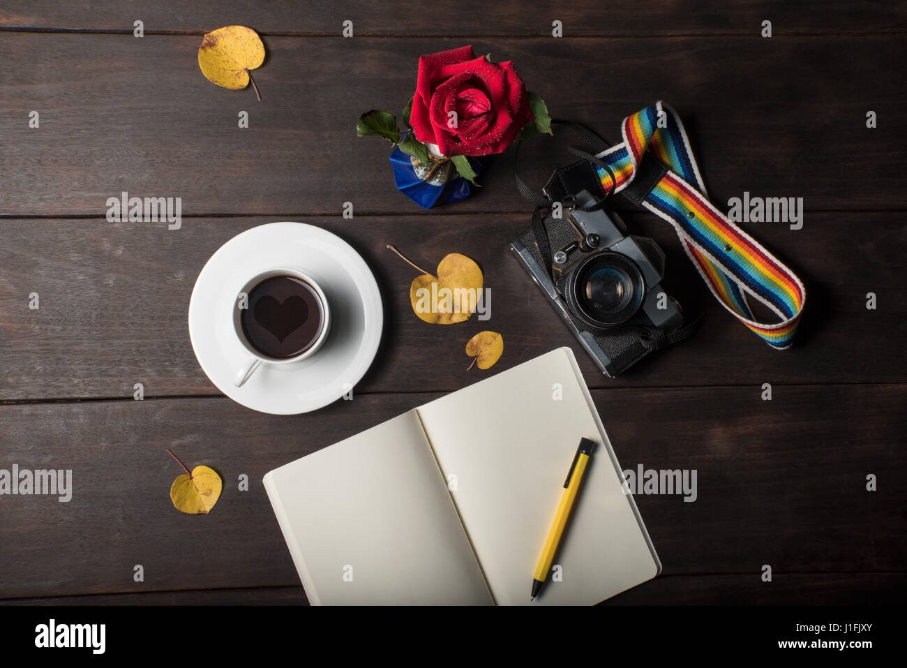 Red Rose, cuore nella tazza di caffè, fotocamera, yellow leaf, notebook e penna su tavola, in stile vintage Foto Stock