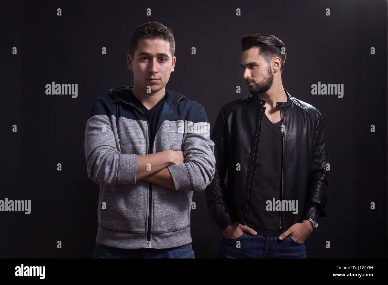 Due giovani uomini adulti, che pongono, abiti casual. Sfondo nero, studio. Foto Stock