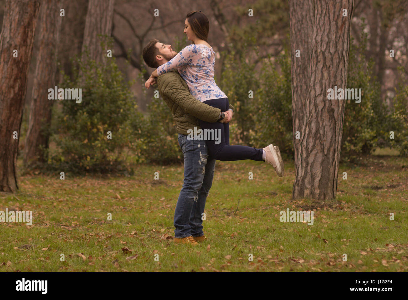 Coppia giovane uomo fidanzato holding ragazza ragazza in armi baciare. In inverno il parco all'aperto boschi giorno Foto Stock