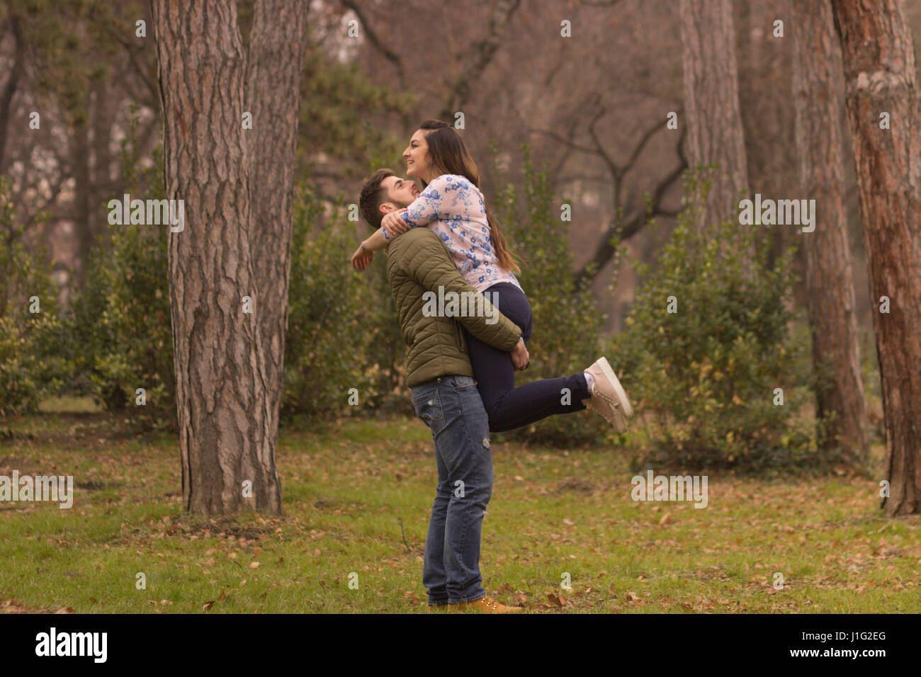 Coppia giovane uomo fidanzato holding ragazza ragazza a bracci. In inverno il parco all'aperto boschi giorno Foto Stock