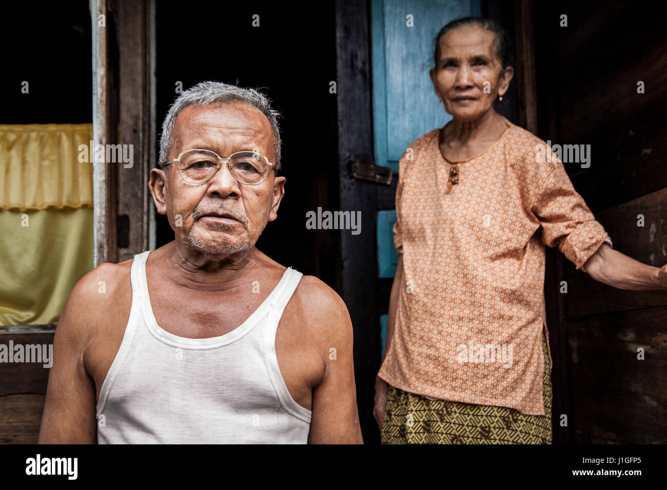 Anziani e umile giovane indonesiano, due anziani cercando deluso in piedi in ingresso alla loro povera e umile casa Foto Stock