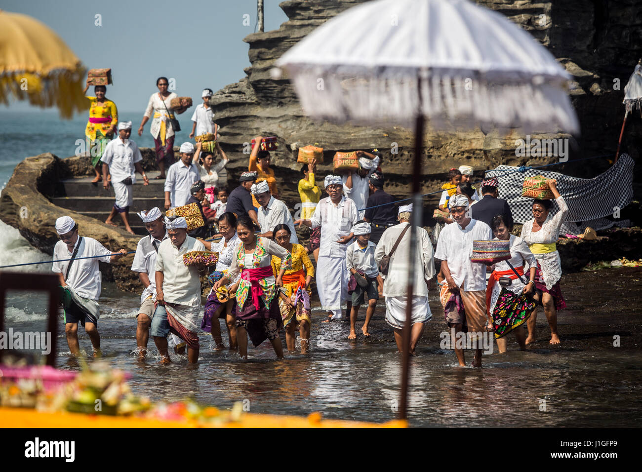 Pellegrini guadare attraverso l'acqua marina a Tanah Lot Temple di Bali con il cerimoniale di offerte alla divinità Indù al rock antico tempio di Pura Luhur Foto Stock