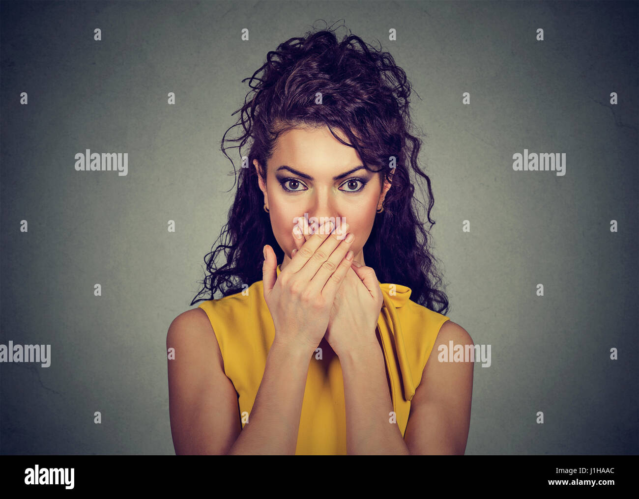 La donna si copre la bocca con le mani guardando la fotocamera Foto Stock