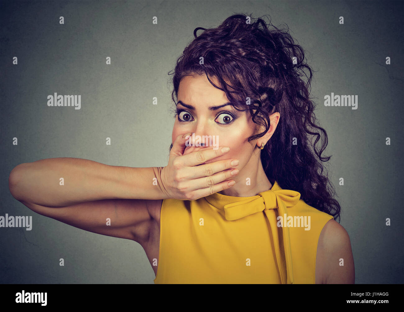 Closeup ritratto di paura giovane donna che copre con la mano la sua bocca isolato sul muro grigio sfondo Foto Stock