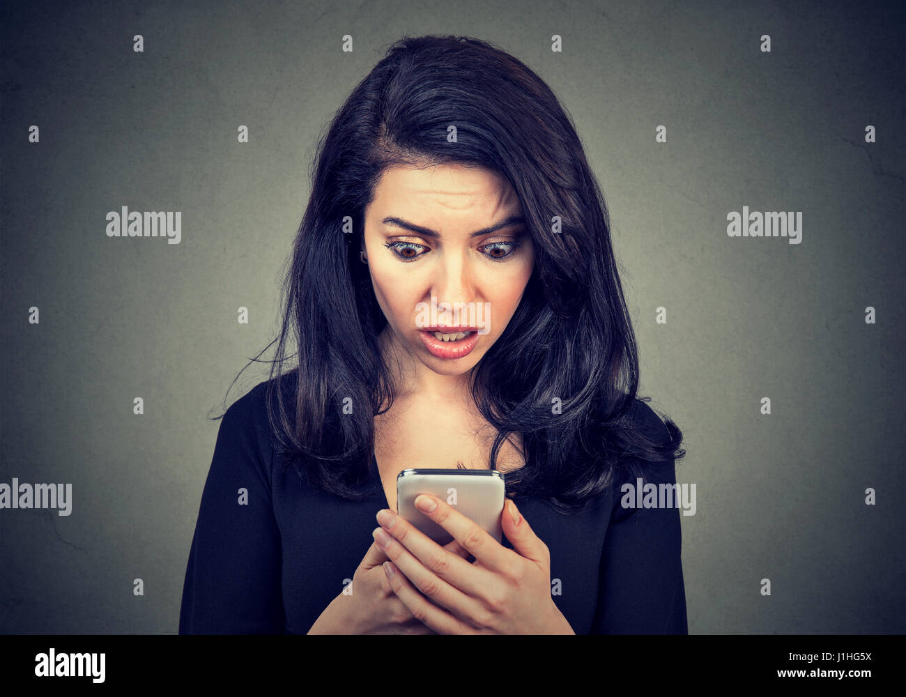 Sottolineato scioccato donna guardando cellphone preoccupato con cattivo messaggio news ha ricevuto isolato su sfondo grigio. Negativo emozione umana sensazione rea Foto Stock