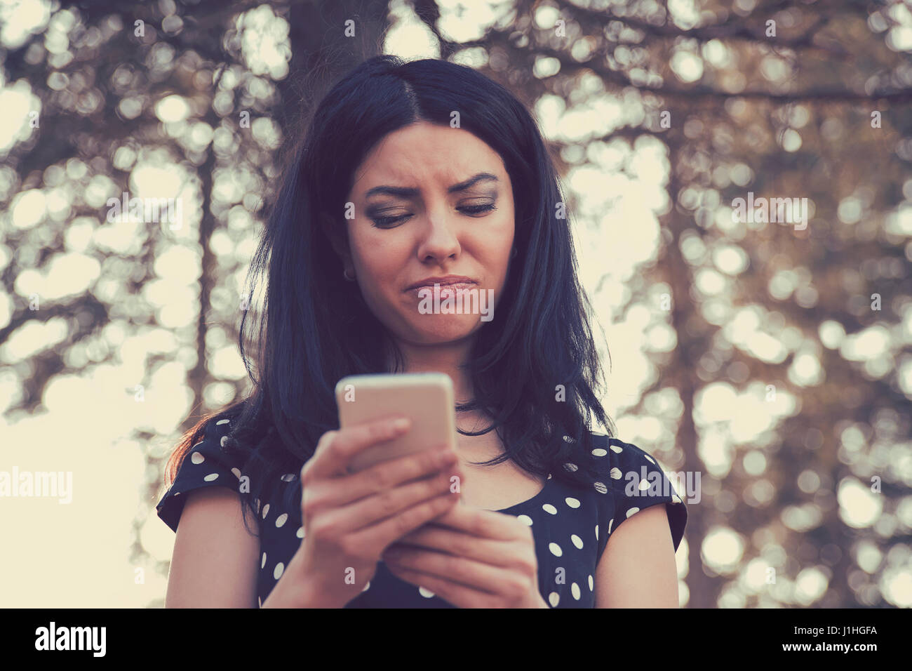 Arrabbiato donna guardando il suo telefono cellulare in piedi all'aperto in un parco Foto Stock
