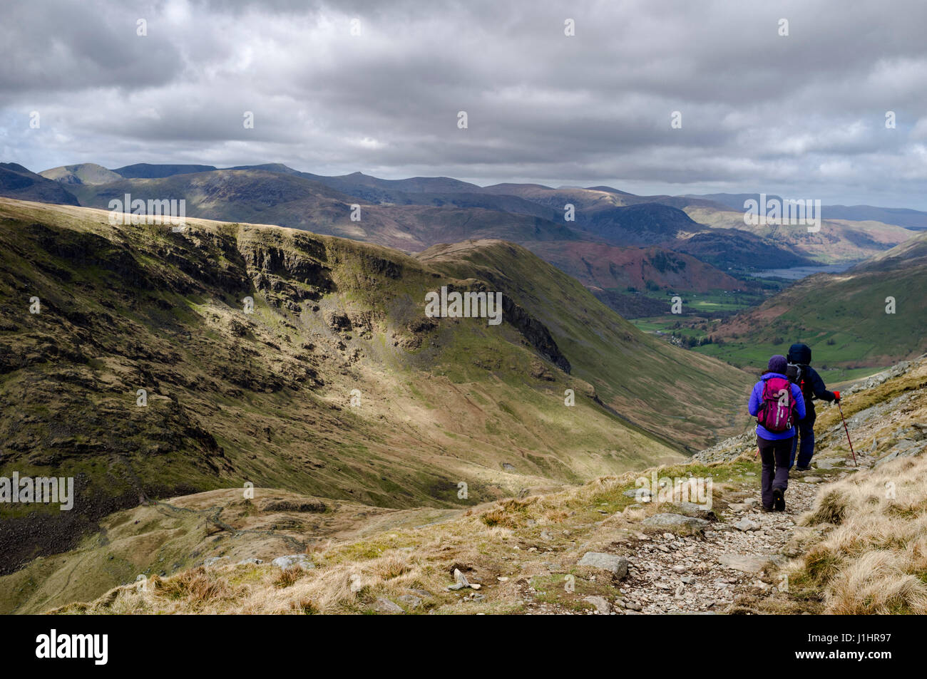Maschio e femmina escursionisti discendente dalla High Street in pascoli fondo verso Hartsop, Patterdale e Ullswater nel distretto del Lago Foto Stock