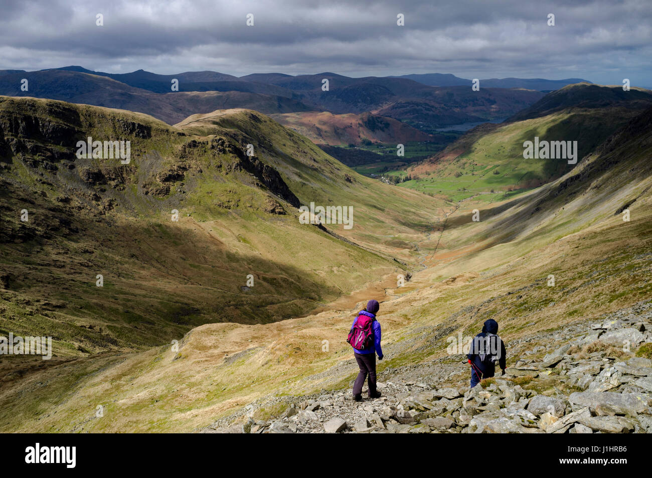 Maschio e femmina escursionisti discendente dalla High Street in pascoli Parte inferiore a forma di U verso valle Hartsop, Patterdale e Ullswater nel distretto del Lago Foto Stock