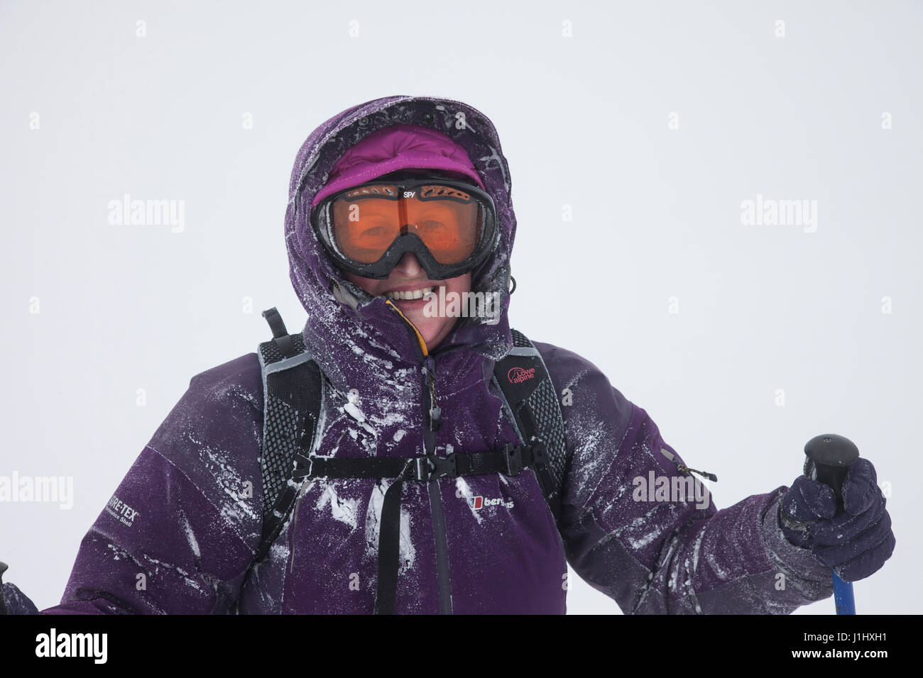 Sorridente donna di mezza età che indossa le attrezzature utilizzate all'aperto e di godere di condizioni di tempo di inverno in montagna di Cumbria Inghilterra England Regno Unito Foto Stock