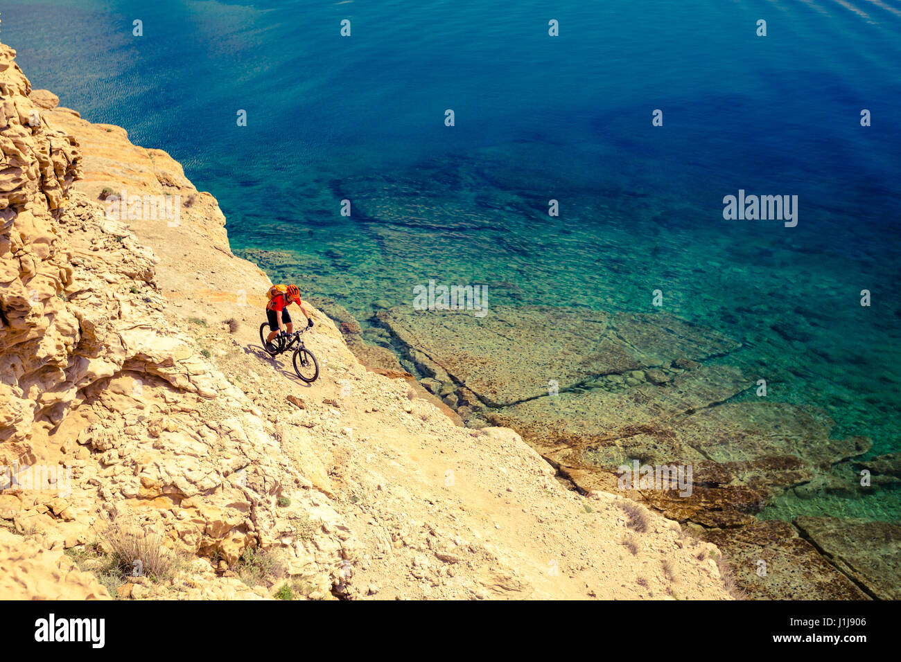 Mountain biker in sella sulla bici in estate ispiranti montagne e mare paesaggio. Uomo MTB ciclismo su pista di enduro la via al mare e rocciosi sterrati pat Foto Stock