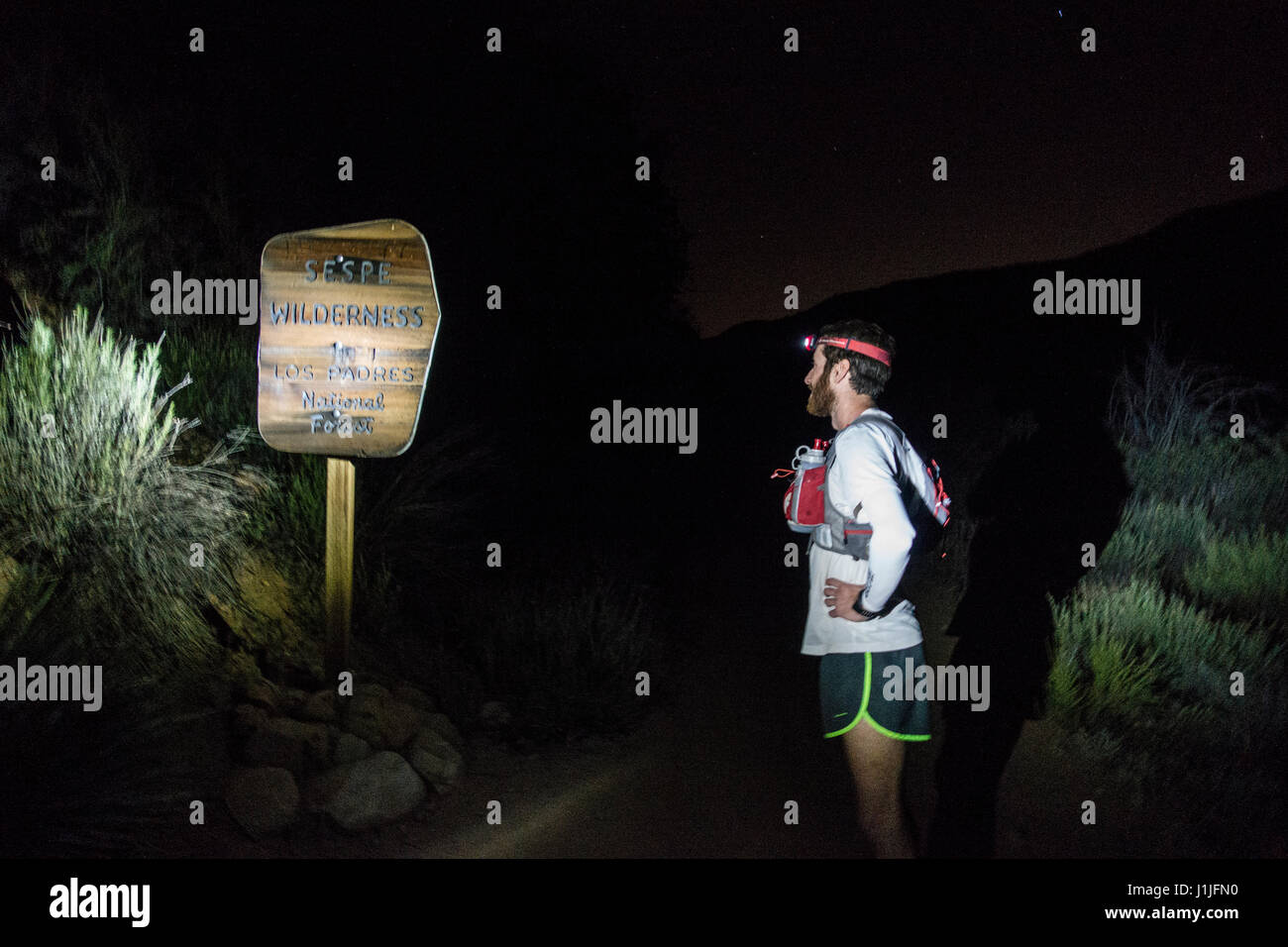 Un trail runner in una notte buia splende il suo proiettore su un segno che segna l'entrata al Sespe deserto in Ojai, California. Foto Stock