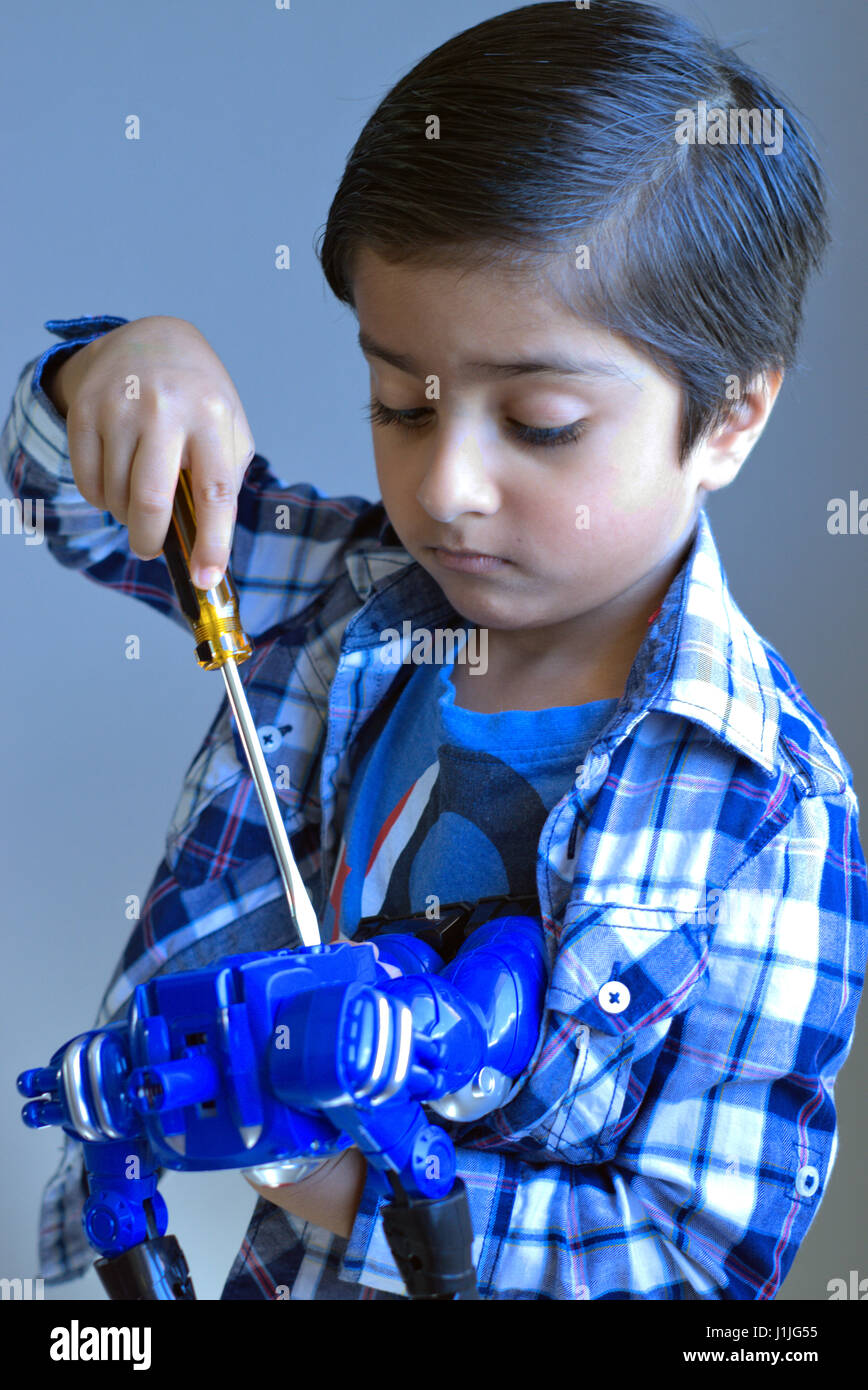 Il capretto con cacciavite guardando giù il fissaggio di un giocattolo. Il capretto con gli strumenti di lavoro che fissa le cose. Bambino occupato cosa di fissaggio. Foto Stock