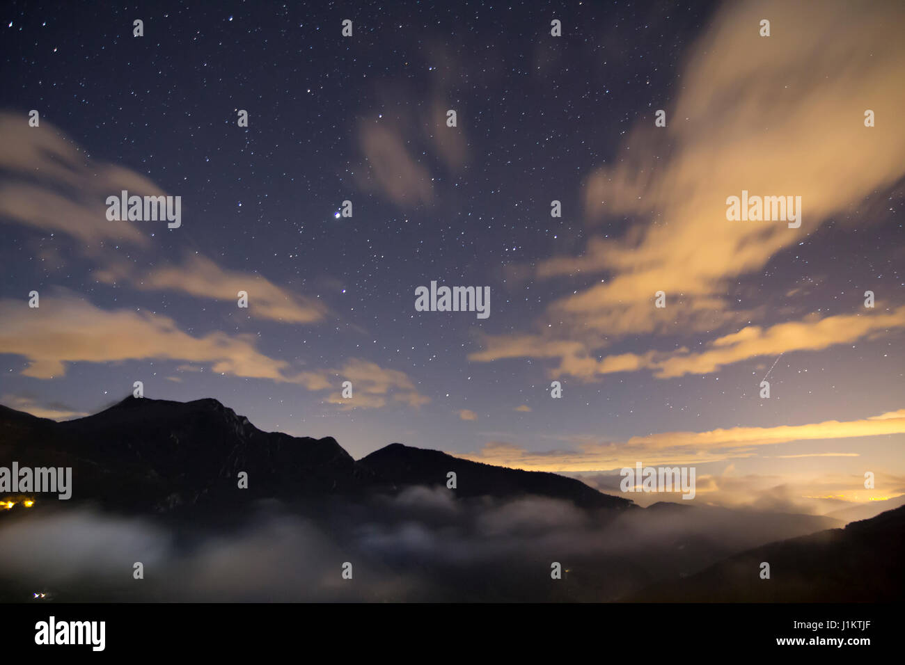 Paesaggio notturno con stelle e Villaggio illuminato in montagna Foto Stock