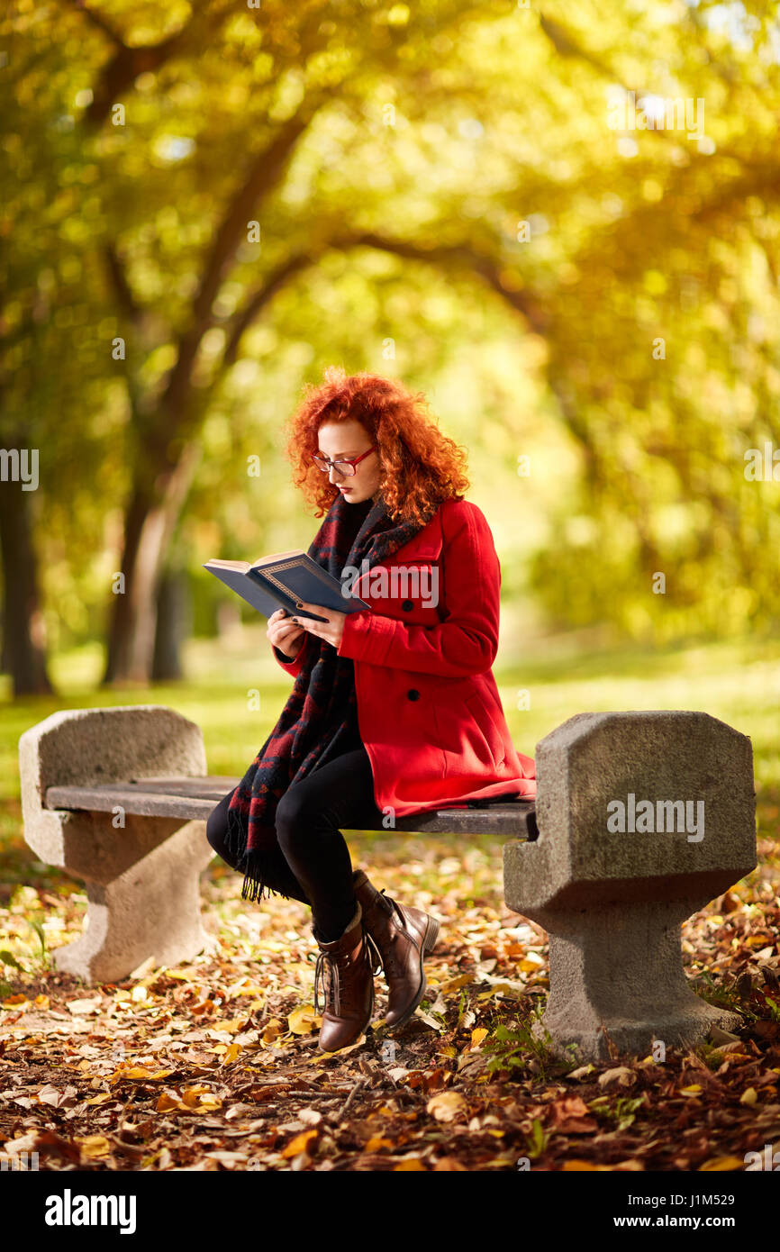 Redhead donna leggere il libro nel parco in autunno Foto Stock