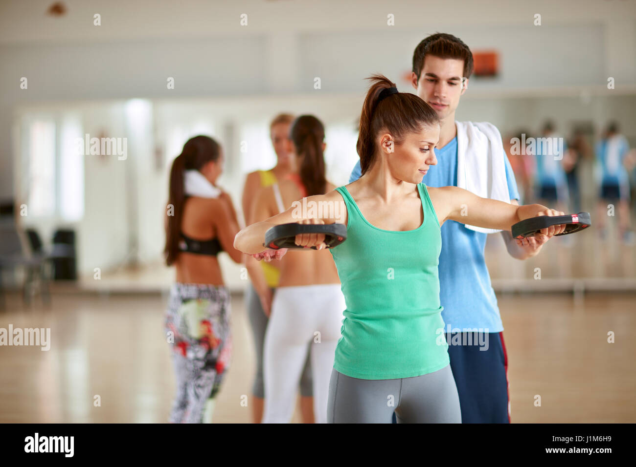Trainer maschio consente di giovane donna mentre i bracci di pratica con attrezzature per esercizi in palestra Foto Stock