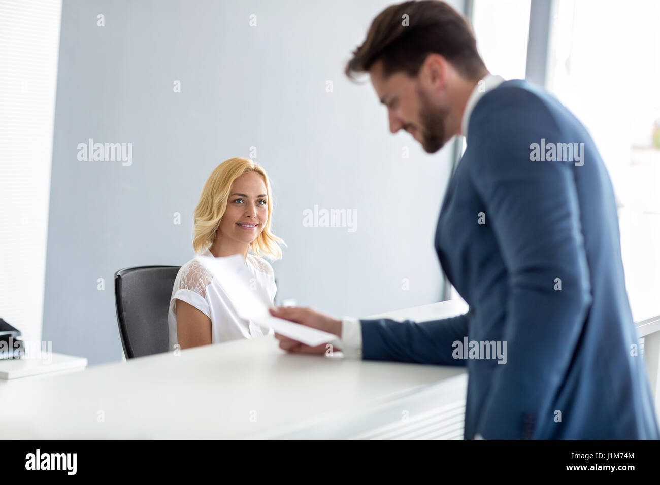 Giovane bella femmina receptionist guarda bello imprenditore al banco di controllo Foto Stock