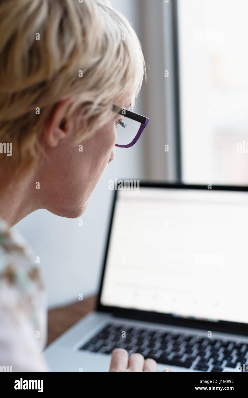 Vista posteriore della femmina in bicchieri seduto e lavorando su laptop su sfondo sfocato. Foto Stock