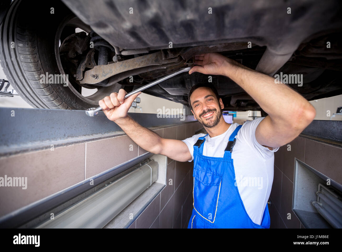 Felice di lavoro meccanico sulla ruota sotto l'auto Foto Stock