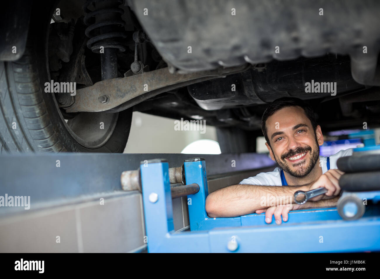 Maschio di lavoro meccanico sotto la vettura sorridente Foto Stock