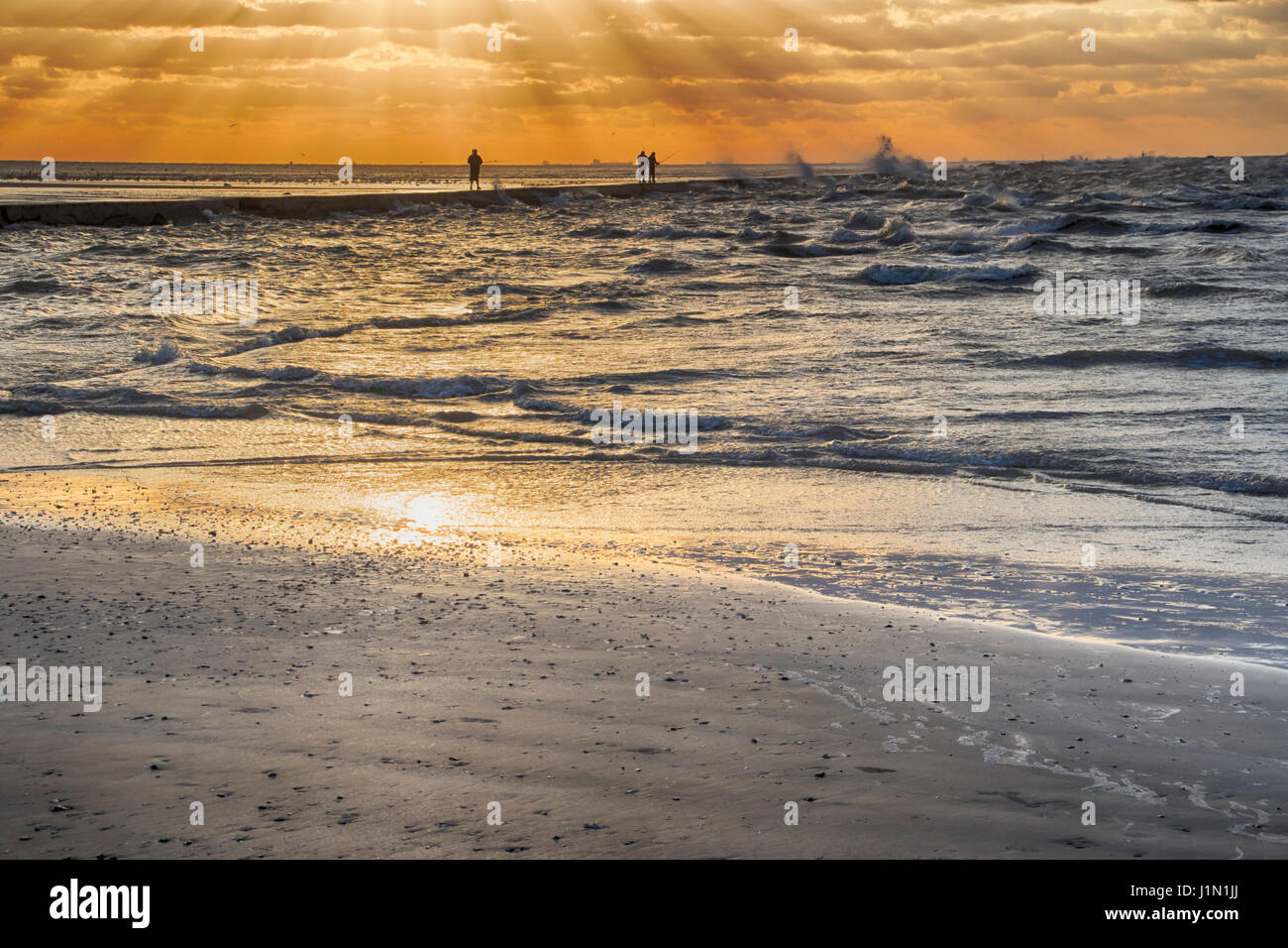 I pescatori sfidando un ventoso e umido con sunrise onde che si infrangono sulla Galveston East Beach Foto Stock