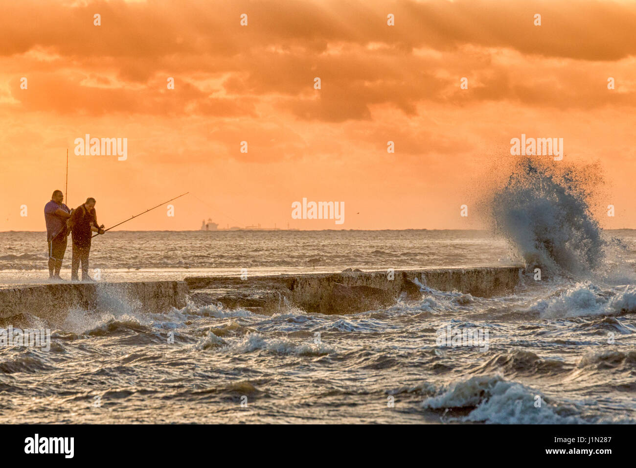 La pesca in mezzo drammatico il vento e le onde a sunrise in Galveston East Beach. Foto Stock