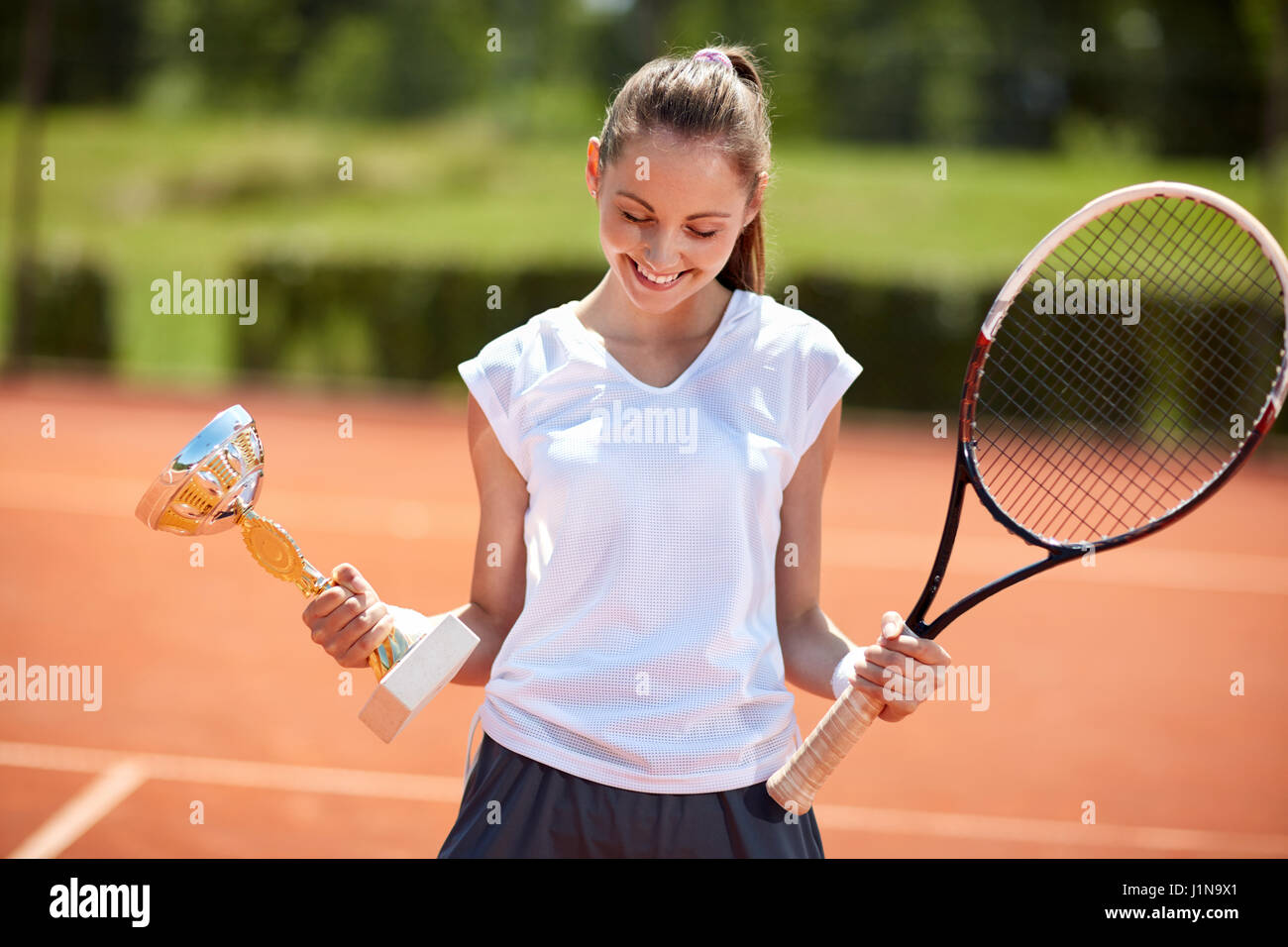 Timida ragazza giovane con calice sul campo da tennis Foto Stock