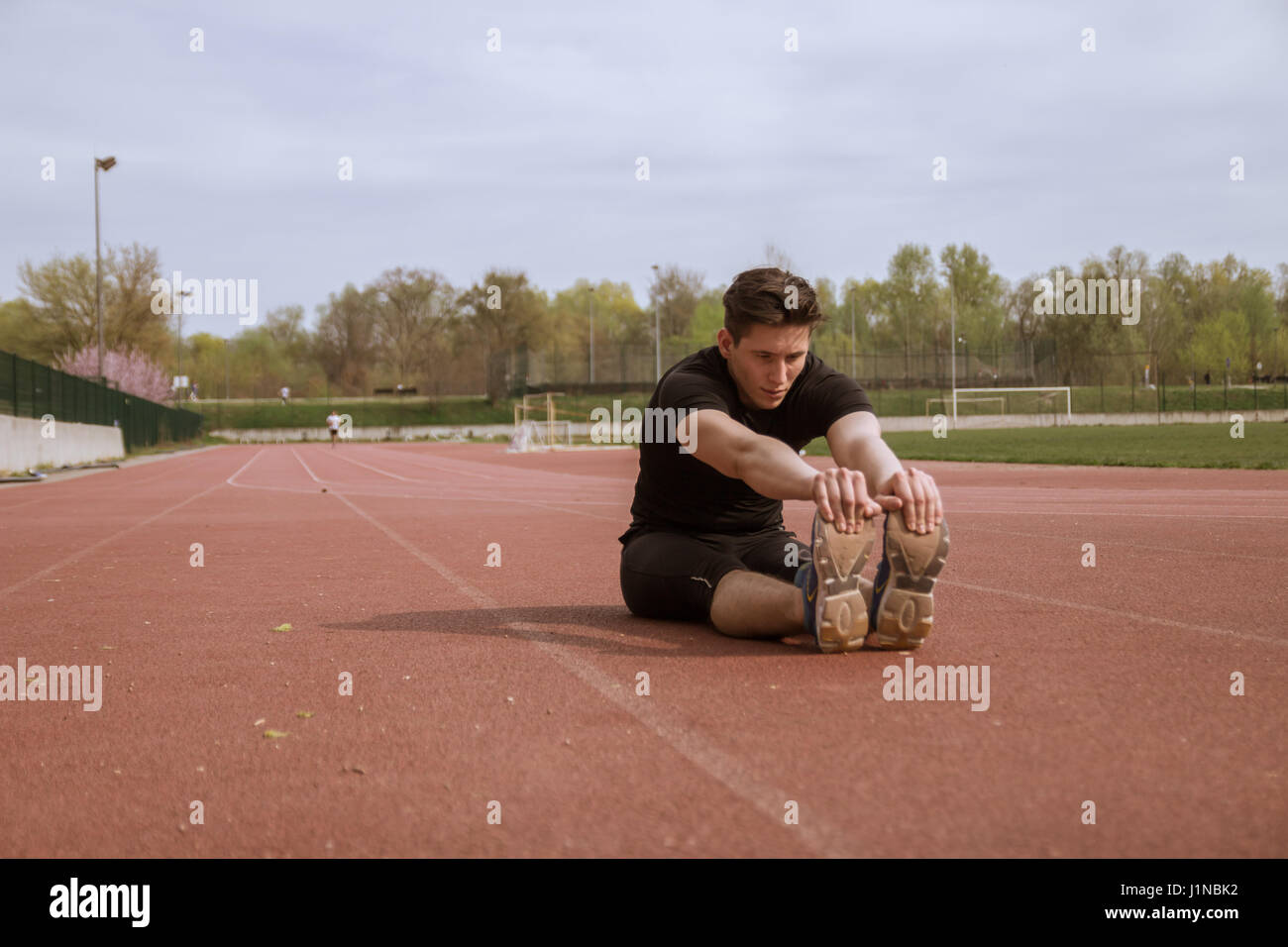 Un giovane uomo, atleta fitness, stretching di due gambe, all'aperto, binari di scorrimento Foto Stock