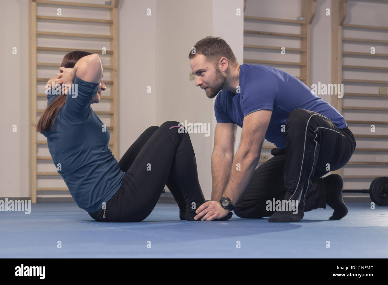 Un giovane uomo solo, trainer fitness istruttore una giovane donna solo esercitare, in interni abs, tenendo i piedi Foto Stock
