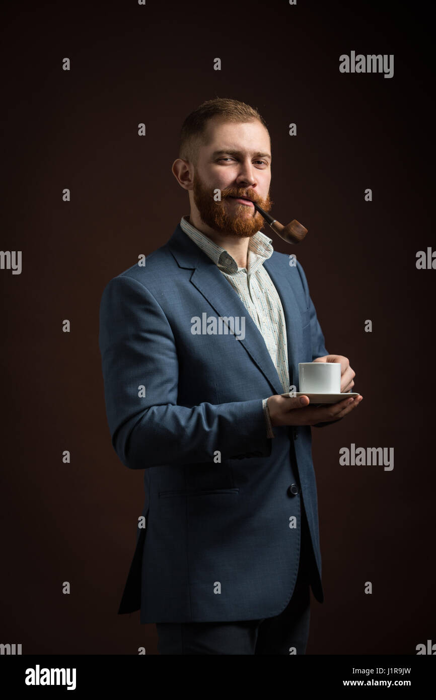 Ritratto di uomo bello con zenzero barba holding tazza di caffè mentre il tubo di fumo Foto Stock
