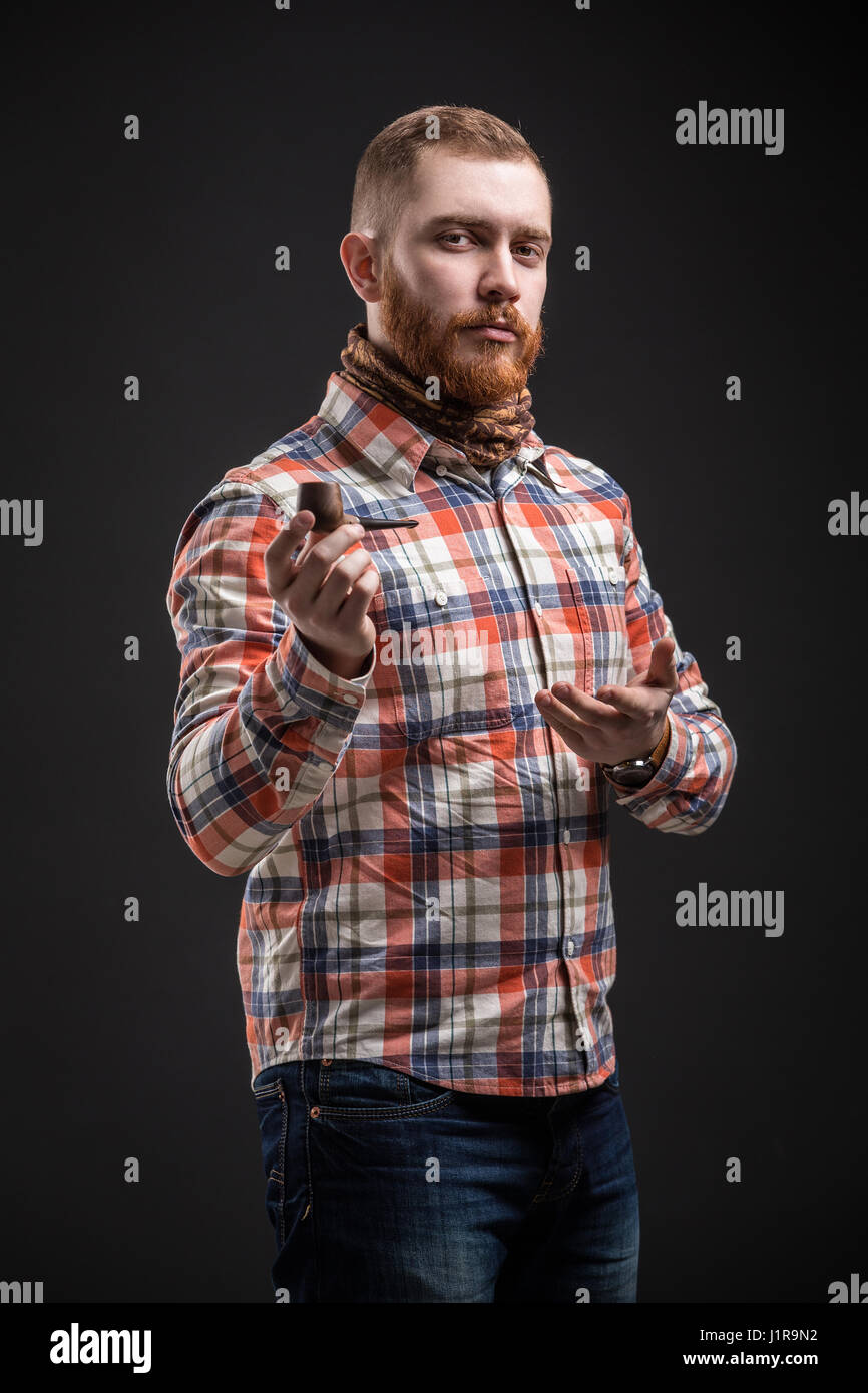 Ritratto di bello uomo barbuto in verifica shirt Presentazione tubo di fumo, Studio shot, isolato Foto Stock